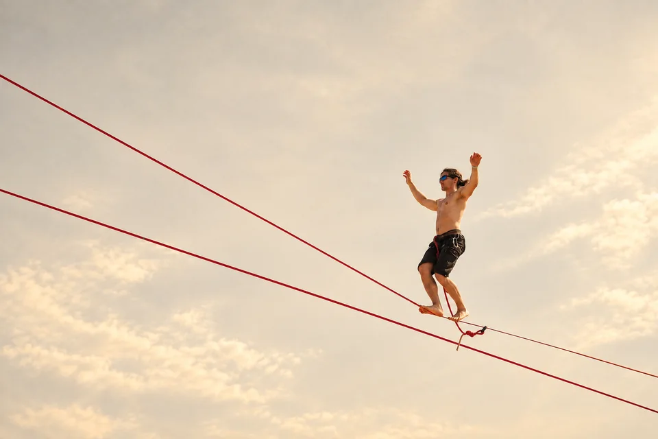 A person balancing on a slackline against a cloudy sky.
